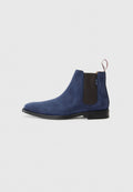 Marineblaues Wildleder-Ankle-Boot mit elastischen Seitenpaneelen, einem Ziehhilfe, abgerundetem Zehenbereich und einer schwarzen Gummisohle. Glatte Textur mit minimaler Verzierung.