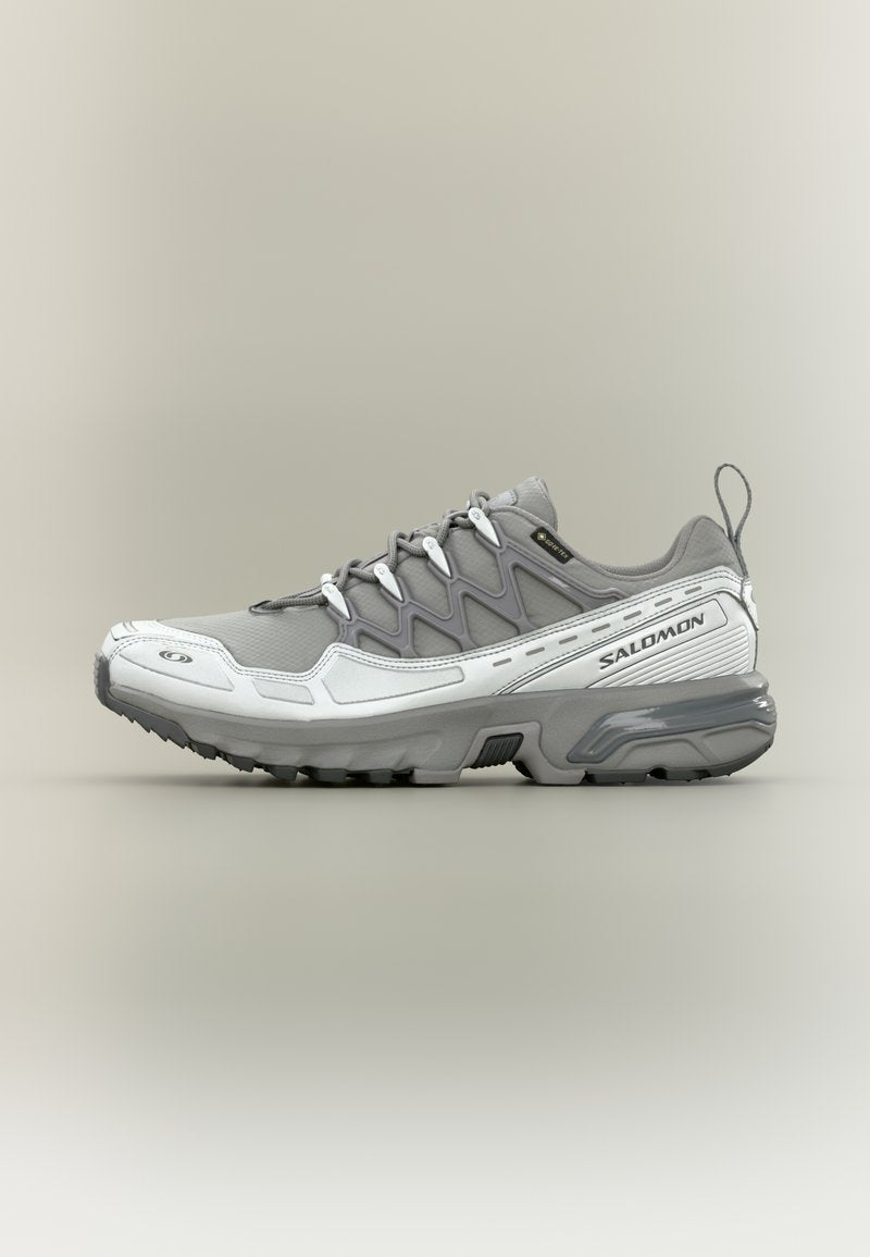 Grauer Sportschuh mit strukturiertem Obermaterial, reflektierenden Akzenten und gedämpfter Sohle. Verfügt über ein Schnürdesign und eine Zuglasche an der Rückseite.