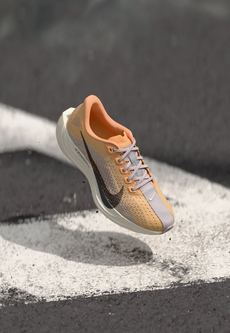 Nike-Laufschuh mit atmungsaktivem Mesh-Obermaterial in Hellgrau und Orange, mit schwarzem Swoosh-Logo und einer gepolsterten weißen Sohle.
