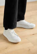 Weißlederen Low-Top-Sneaker mit Schnürung, abgerundeter Zehenpartie und minimalistischem Design. Kombiniert mit schwarzen, schmal zulaufenden Jeans.