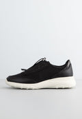 Schwarze Sportschuhe aus einer Kombination von Mesh-Gewebe und synthetischem Leder, mit einem Slip-On-Design und einer weißen Gummisohle mit strukturierten Akzenten.