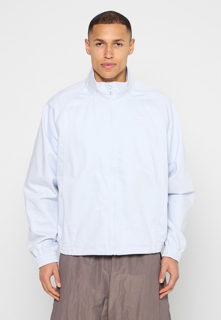 Hellblauer Reißverschlussjacke mit hohem Kragen, elastischen Bündchen und kontrastierendem Material. Mit weißem Nike-Logo auf der Brust.