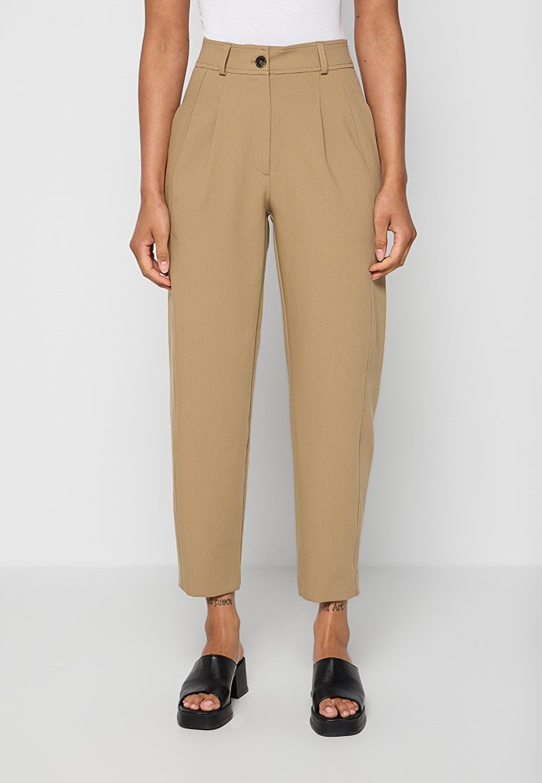 Beige, hoch taillierte, schmal zulaufende Hose mit Falten, Knopfverschluss, getragen mit schwarzen offenen Sandalen mit Blockabsatz und einem weißen Oberteil.