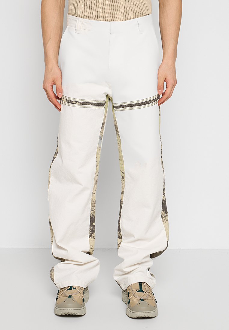 Weiße Cargo-Hosen mit Camouflage-Seitenpaneelen, die eine entspannte Passform und sichtbare Nähte aufweisen. Taschen vorhanden, präsentiert vor einem neutralen Hintergrund.