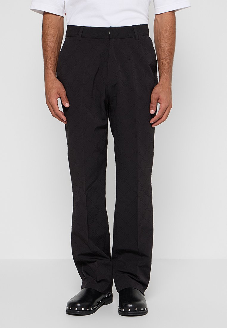 Schwarze Hose mit Rautenmuster, gewebter Stoff, gerade Passform und seitlichen Taschen, kombiniert mit schwarzen Schuhen mit Metallnieten.