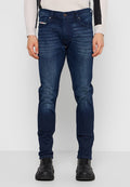Dunkelblaue Denim-Jeans mit schlanker Passform, sichtbaren Nähten, Vordertaschen und dezenten Verblassungen. Kombiniert mit schwarzen Schuhen.
