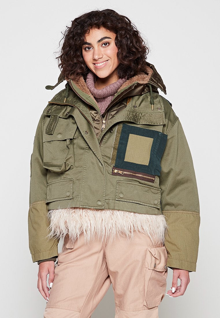 Grüne verkürzte Jacke mit einem Besatz aus Kunstfell, großen Taschen und einem Patchwork-Design in Blau und Khaki. Das Material wirkt strapazierfähig und strukturiert.