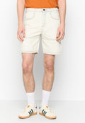 Helle beige Denim-Shorts mit zwei Vorderfächern und Nähten, die auf einen knielangen Schnitt hindeuten. Kombiniert mit weißen Socken und grün gestreiften Sneakers.