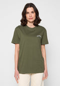 Frau mit schulterlangem braunem Haar, die ein olivgrünes T-Shirt mit kurzen Ärmeln und weißem Text auf der Brust sowie hellbeige Hosen trägt.