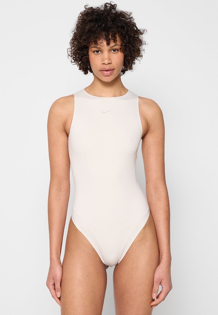 Hellbeiger Einteiler-Badeanzug mit hohem Kragen und ärmellosem Design. Glatte Textur mit einem dezenten Nike-Logo auf der Brust.