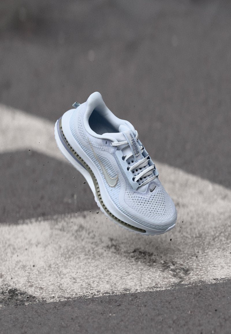Helles blaues Sport-Schuhwerk mit Mesh-Obermaterial, weißen Schnürsenkeln und grauen Akzenten. Verfügt über eine gepolsterte Sohle und ein auffälliges Swoosh-Logo.
