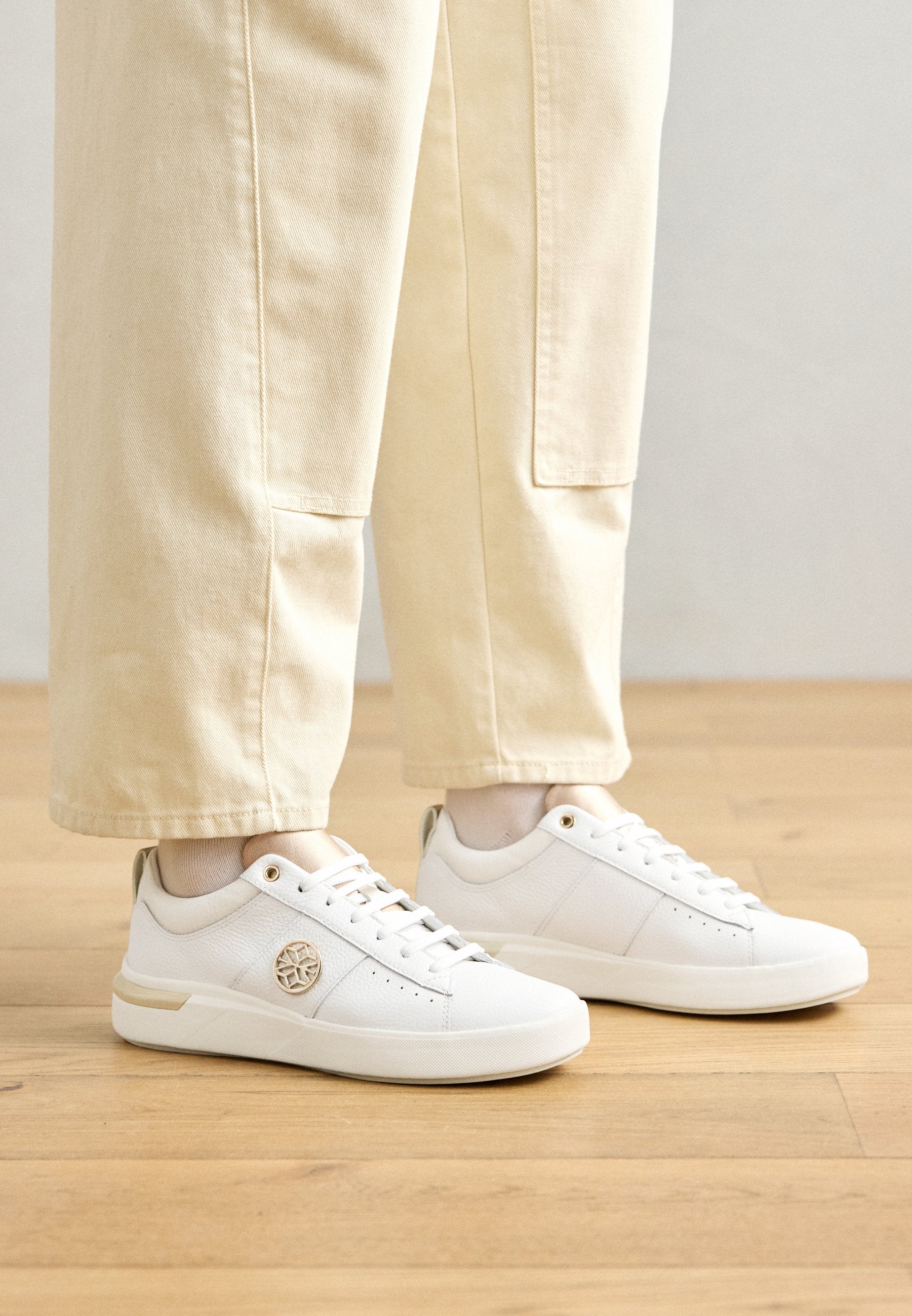 Weiße Sneaker aus glattem Leder mit runder Zehenform, goldenen Akzenten und Schnürdesign. verfügen über ein Logo an der Seite und feine Perforationen.