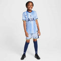 Helles blaues Fußballtrikot mit vertikalen Streifen, schwarzem "AIA"-Logo, marineblauen Akzenten und passenden Shorts. Schwarze Stollenschuhe und knielange marineblaue Socken.