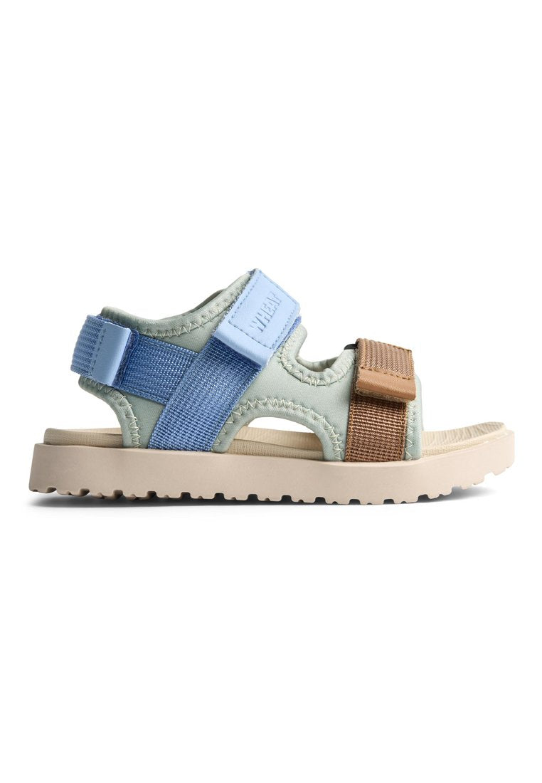 Blaue und grüne Sandale mit verstellbaren Riemen, strukturiertem Stoff und einer beigen Gummisohle mit profiliertem Muster für besseren Halt.