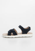 Navy blauer Wildledersandal mit Riemen und Klettverschluss. Weiße Gummisohle, gepolstertes Fußbett und dekoratives Blumendetail. Offene Zehenpartie und offener Rücken.