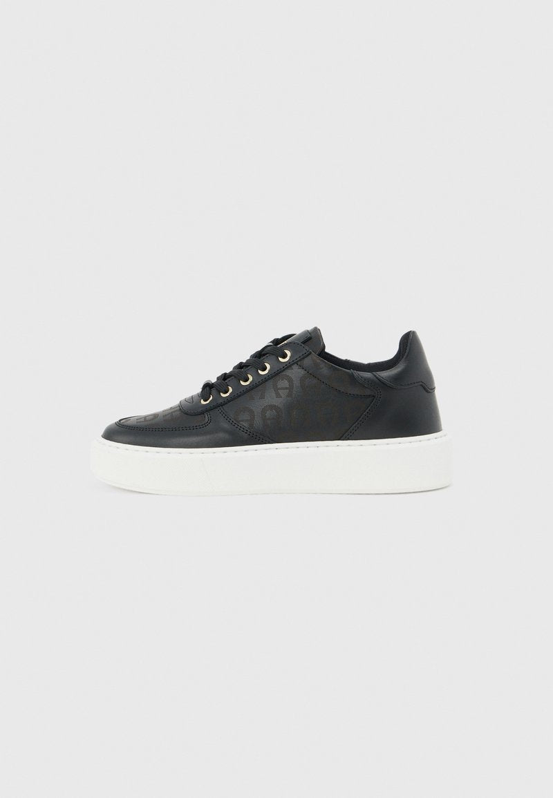 Schwarzer, flach geschnittener Ledersneaker mit dezentem Monogramm-Muster, schwarzen Schnürsenkeln mit goldenen Ösen und dicker weißer Plateausohle.