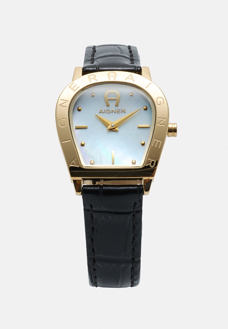 Goldfarbene Aigner-Uhr mit abgerundetem trapezförmigem Zifferblatt, weißem Zifferblatt, goldenen Zeigern und Markierungen, schwarzem Lederarmband mit Steppnähten.