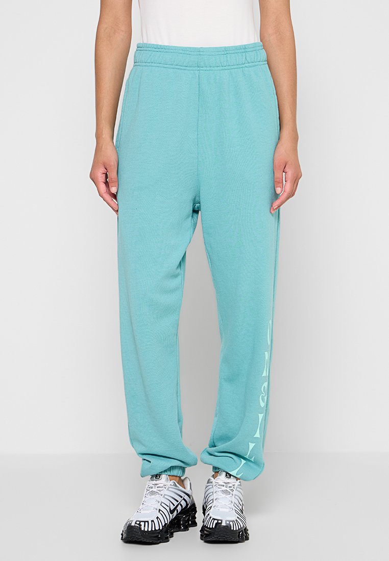 Türkise Sweatpants mit lockerer Passform, ausgestattet mit einem elastischen Bund und seitlichen Taschen. Das linke Bein hat ein weißes grafisches Druckdetail.