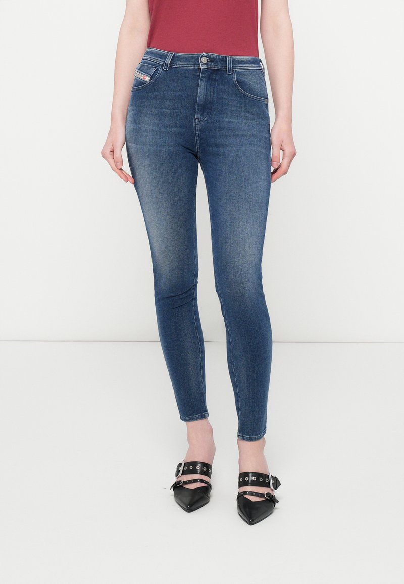 Schlanke blaue Jeans in dunkler Waschung mit einer mittelhohen Taille, Fünf-Taschen-Design und minimaler Ausbleichung. Begleitet von schwarzen spitzen Schuhen.