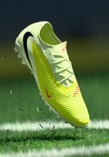 Fußballschuh mit einem leuchtend gelben Obermaterial, das mit strukturierten Rillen versehen ist, weißer Sohle, schwarzen Akzenten und pinken Details auf dem Swoosh und an der Seite.