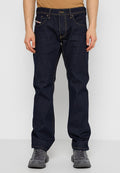 Mann in dunkelblauen, gerade geschnittenen Jeans mit kontrastierenden Nähten und grauen Sportschuhen, der vor einem weißen Hintergrund steht.