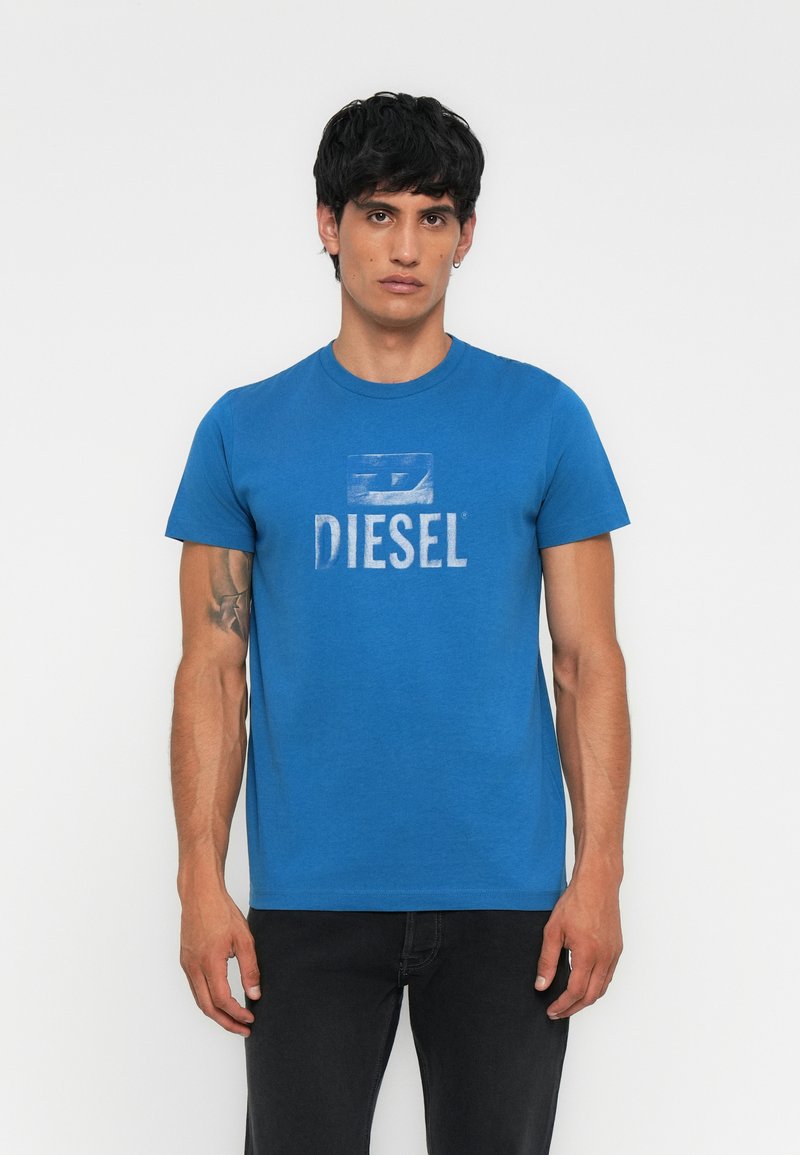 Blaues Baumwoll-T-Shirt mit einem verblassten weißen "DIESEL"-Logo in der Mitte, Rundhalsausschnitt und kurzen Ärmeln, kombiniert mit schwarzen Jeans.