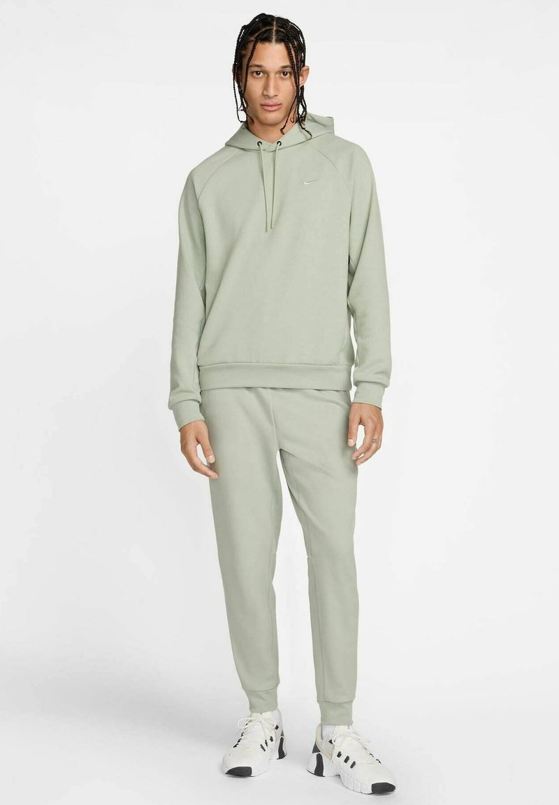 Hellgrüner Sweatshirt mit verstellbarer Kapuze und gerippten Bündchen, kombiniert mit passenden Sweatpants. Weiße und schwarze Sportschuhe vervollständigen das Outfit.