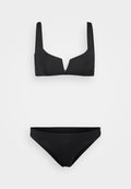 Schwarzes Bikiniset mit einem Bralette-Oberteil mit breiten Trägern und einem V-förmigen Ausschnitt, kombiniert mit klassischen Bikinihöschen. Glatte Textur.