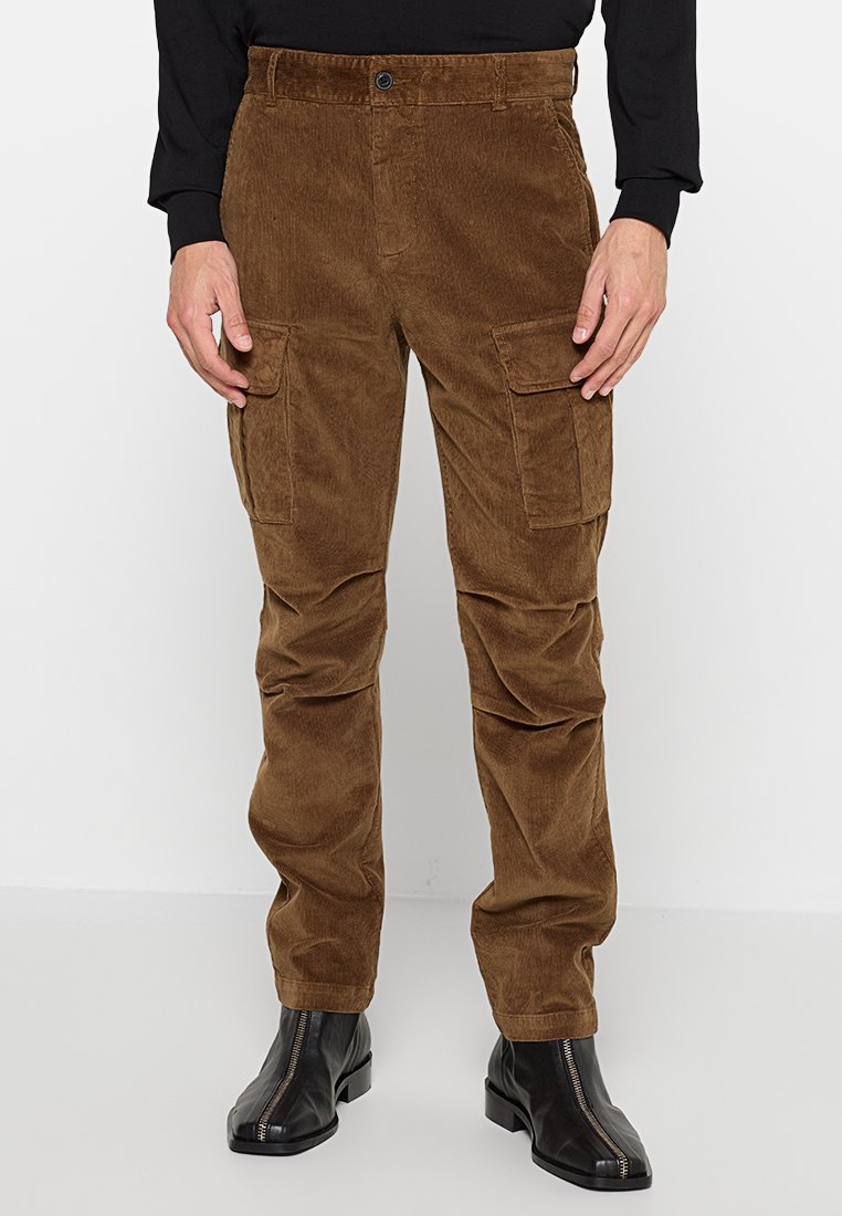 Braune Kordhosen im Cargo-Stil mit mehreren Seitentaschen, einem Knopfverschluss und geradem Bein, kombiniert mit schwarzen Knöchelstiefeln.