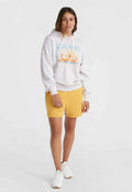 Grauer Hoodie mit Kalifornien-Passform, kombiniert mit gelben Shorts. Model trägt weiße Turnschuhe. Einfarbiger Hintergrund.