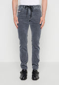 Mann trägt ausgewaschene schwarze Slim-Fit-Jeans mit schwarzen Leder-Doppelschnallen-Schuhen und steht vor einem schlichten hellen Hintergrund.