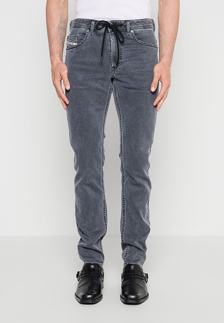 Mann trägt ausgewaschene schwarze Slim-Fit-Jeans mit schwarzen Leder-Doppelschnallen-Schuhen und steht vor einem schlichten hellen Hintergrund.