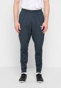 Mann trägt dunkelgraue Nike-Sporthose, weiße Socken, schwarze Spikes, steht vor einem schlichten weißen Hintergrund.