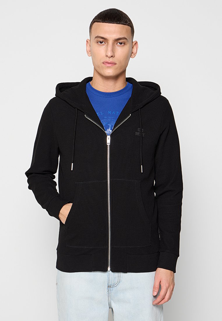 Schwarze Zip-Hoodie aus strukturiertem Material, mit Fronttaschen, verstellbaren Kordeln und einem dezenten Logo auf der linken Brust.