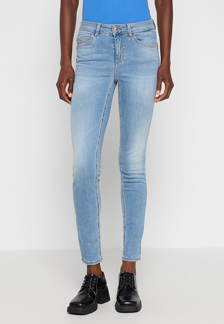 Hellblaue Skinny-Jeans aus Denim, mit normalen Taschen, leichter Verblassung und tailliertem Design. Kombiniert mit schwarzen Schnürschuhen.