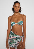 Bikini-Set mit einem trägerlosen Oberteil mit verschnörkeltem Knoten, im grünen und rosa tropischen Muster; kombiniert mit einem Wickelrock, der Palmen zeigt.
