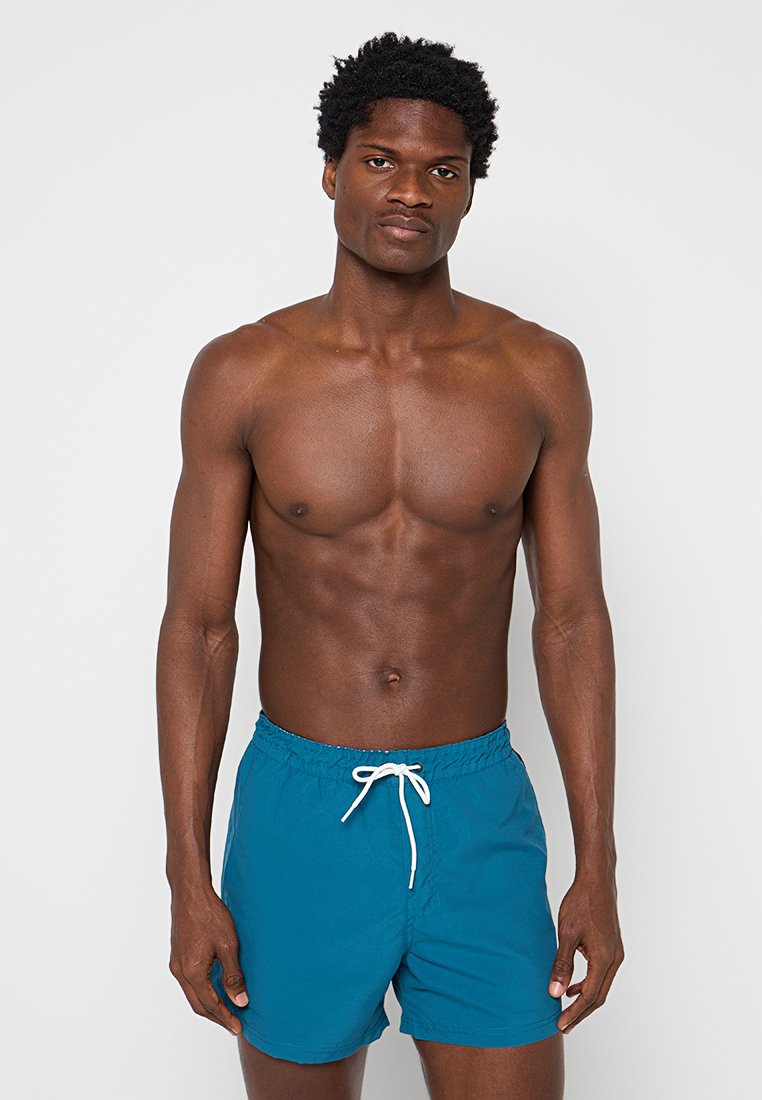 Türkisfarbene Badeshorts aus leichtem Material, mit einem elastischen Bund und weißem Kordelzug sowie einer bequemen Passform.