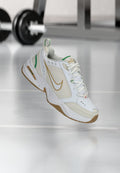 Weiße Sportschuhe mit einem strukturierten Obermaterial aus Leder, goldenem Nike-Swoosh, grünen Akzenten und einer Gummisohle. Verfügt über ein Schnürdesign und einen gepolsterten Saum.
