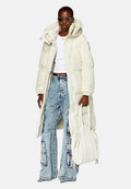 Große Person mit einem langen, cremefarbenen Puffer-Mantel, einem weißen, taillierten Oberteil, ausgewaschenen Cargo-Jeans, dunklen Sonnenbrillen und einer großen weißen Handtasche.