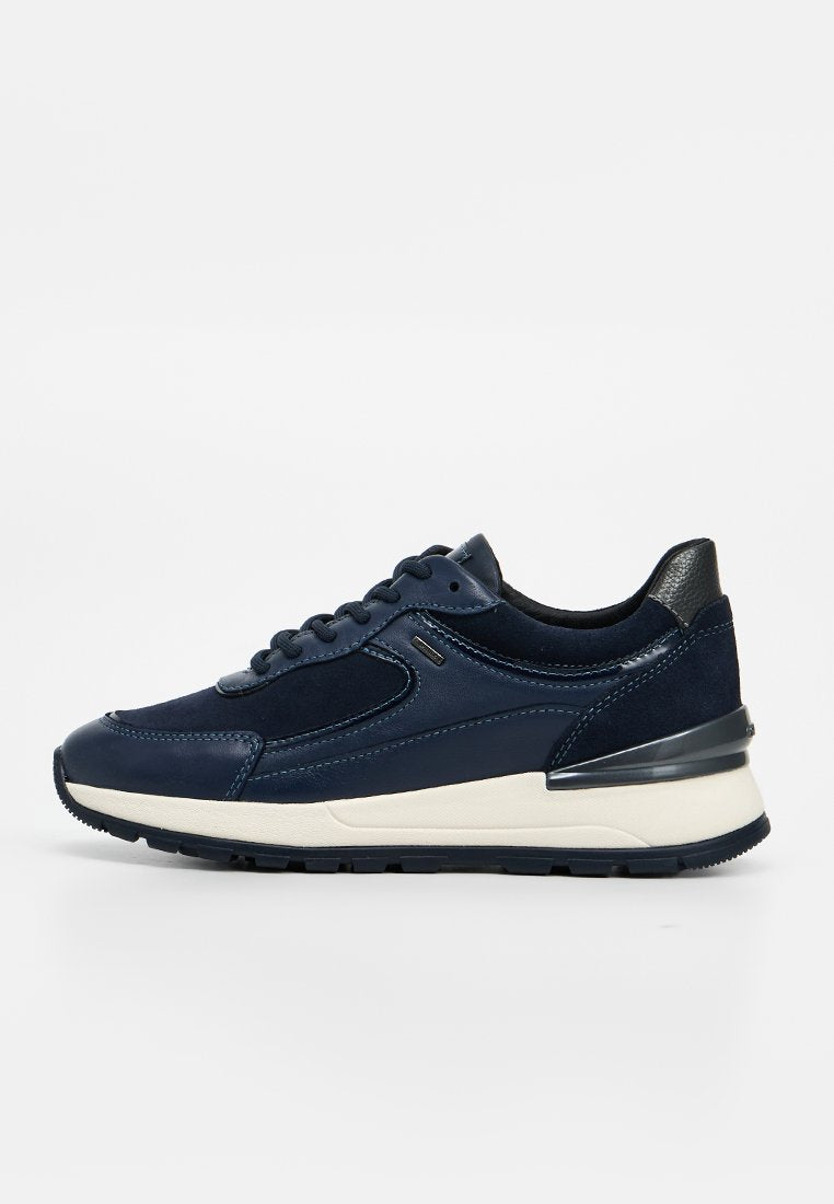 Marineblauer Sneaker mit Schnürverschluss, weißer dicker Sohle und schwarzem strukturiertem Fersendetail, seitlich auf weißem Hintergrund gezeigt.