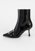 Schwarze Lackleder-Stiefelette mit spitzem Zehenbereich, metallischem Schnallendetail und dünnem hohen Absatz. Glatte Textur mit glänzender Oberfläche.