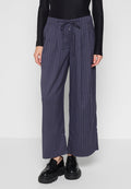 Modell trägt marineblaue, weit geschnittene Nadelstreifenhosen mit Kordelzug und schwarze klobige Loafers vor einem schlichten hellen Hintergrund.