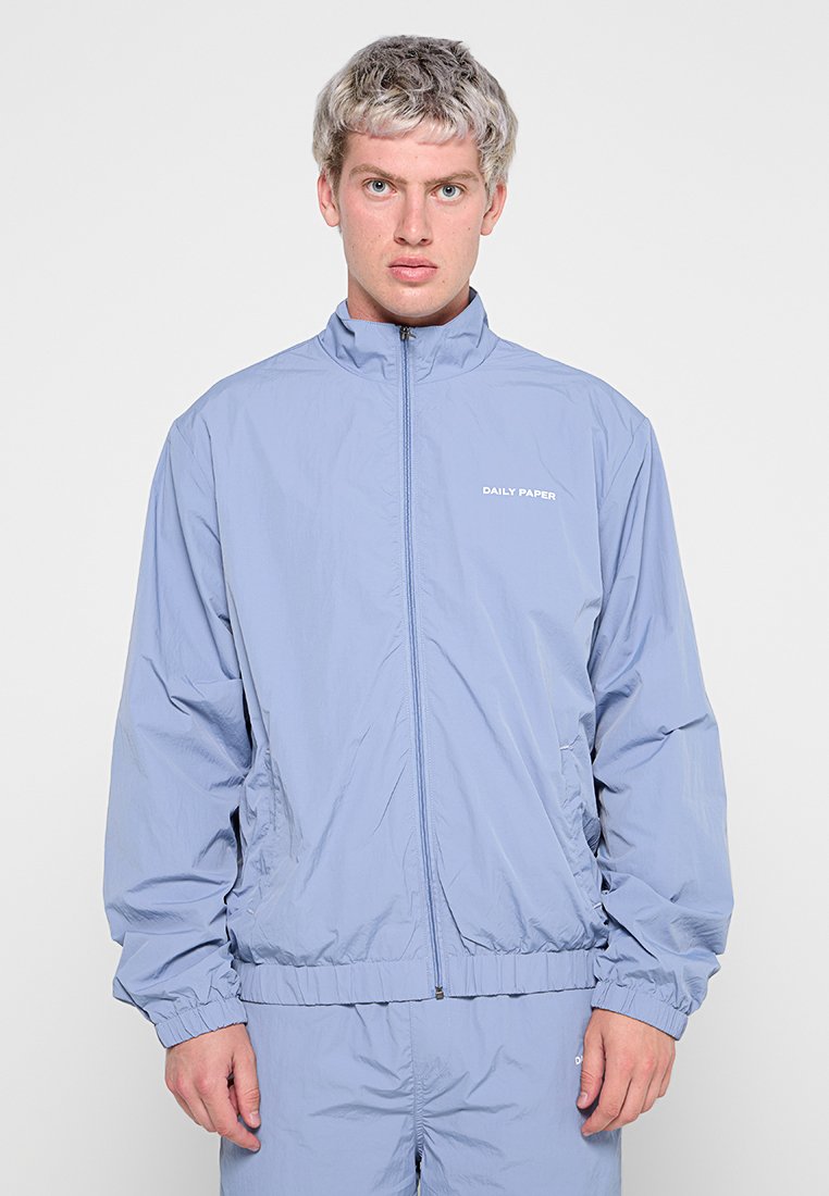 Hellblauer, Reißverschluss-Windbreaker mit Stehkragen, elastischen Bündchen und einem vorderen Logo "DAILY PAPER". Hergestellt aus einem glatten, leichten Stoff.