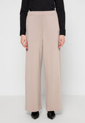 Beige weite Hosen aus weichem Stoff mit flachem Bund, hoher Taille und seitlichen Taschen, kombiniert mit schwarzen spitzen Schuhen.