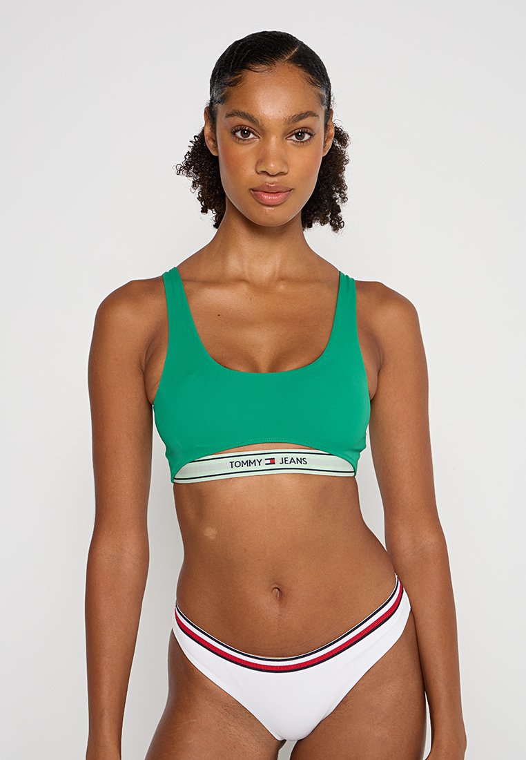 Grünes Crop-Top mit rundem Ausschnitt und breiten Trägern, ausgestattet mit einem weißen Taillenbund mit "TOMMY JEANS"-Logo; kombiniert mit weißen Bikinislips.