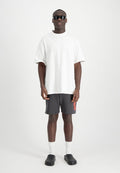 Weißes, übergroßes T-Shirt, graue Shorts mit rotem "ALPHA"-Text, weiße Crew-Socken, schwarze Slipper und schwarze Sonnenbrille.
