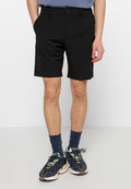 Schwarze Shorts aus elastischem Stoff, mit einem Knopfverschluss vorne und Seitentaschen. Getragen mit marineblauen Socken und gemusterten Turnschuhen.