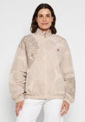 Beige Zip-Jacke mit strukturierten Mustern in dunklerem Beige, elastischen Bündchen und einem kleinen roten Logo auf der Brust.