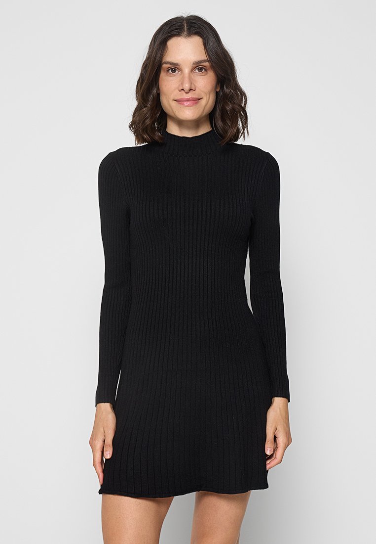 Schwarzes, geripptes Strickkleid mit langen Ärmeln und hohem Kragen. Der Stoff ist texturiert, und das figurbetonte Design läuft etwas an der Taille zusammen.