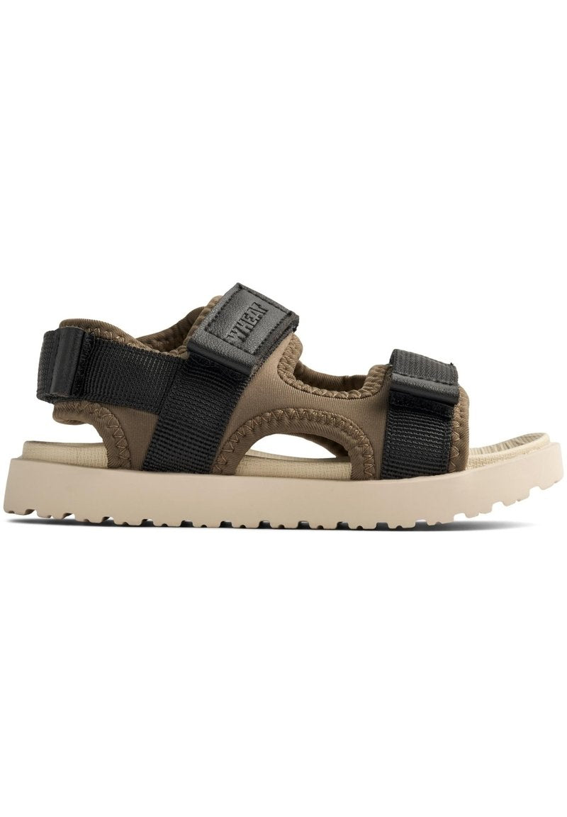 Beige Sandale mit schwarzen verstellbaren Riemen, strukturiertem Obermaterial und einer hellen Gummisohle mit einem Profilmuster für besseren Halt.